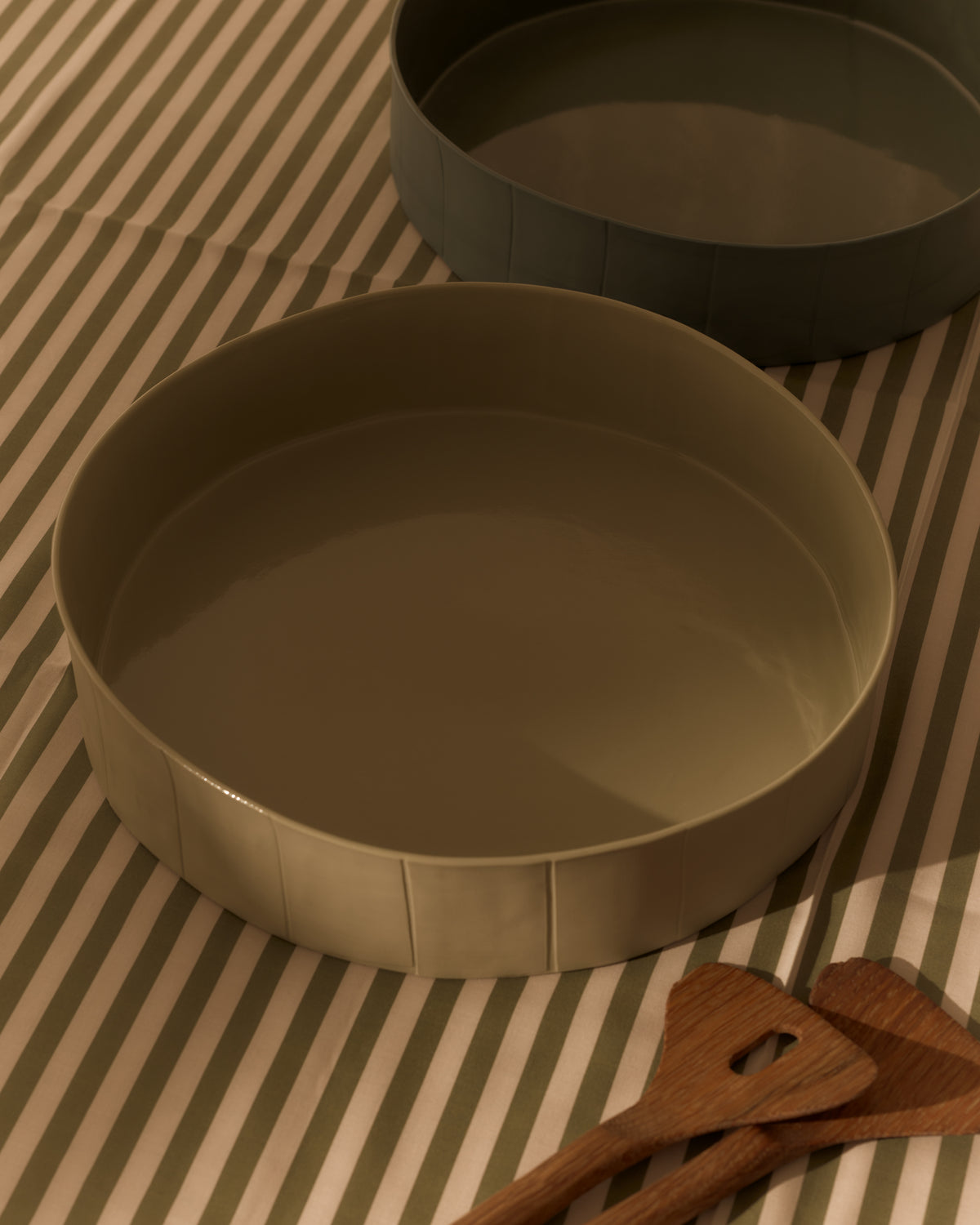Ribbons Large Centrepiece Bowl in Eucalypt Green, with a Dark Forest Green bowl behind, on a striped cloth