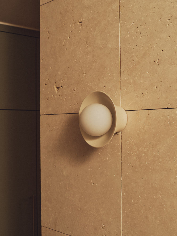 Natural White Pixie Wall Sconce on a travertine wall. Photograph by Sarah Forgie