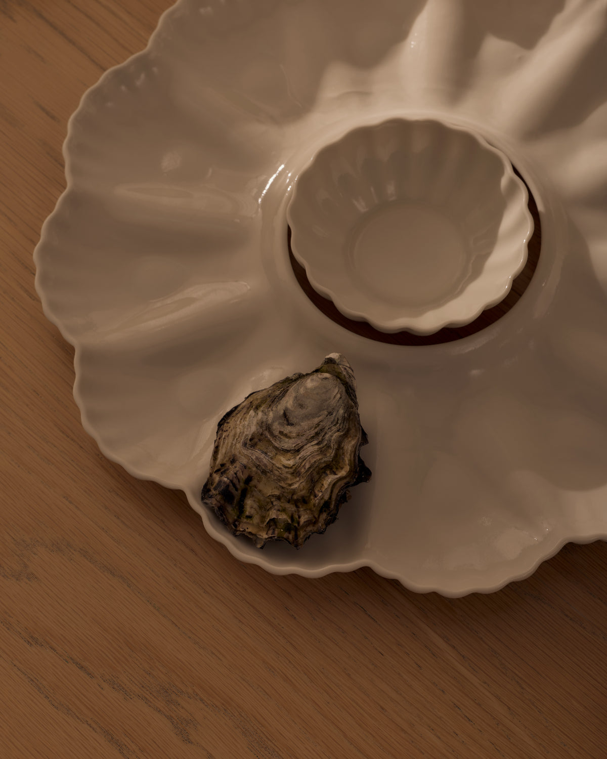 Mother of Pearl Oyster Plate, Dozen, in Natural White with the XS Fern Nesting Bowl, styled on a table. Photograph by Lillie Thompson